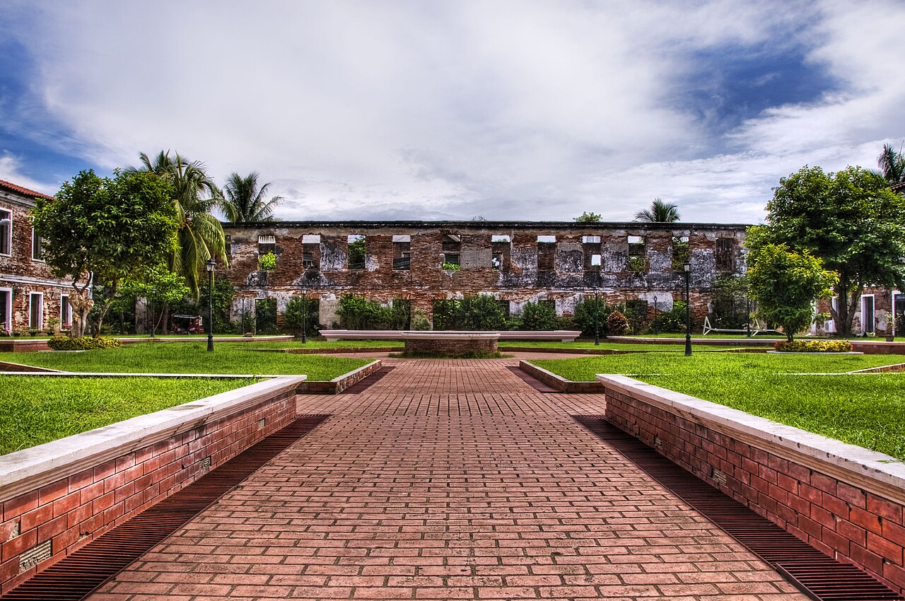 A brick walkway through lawns and palm trees to the walls of an old Spanish fort