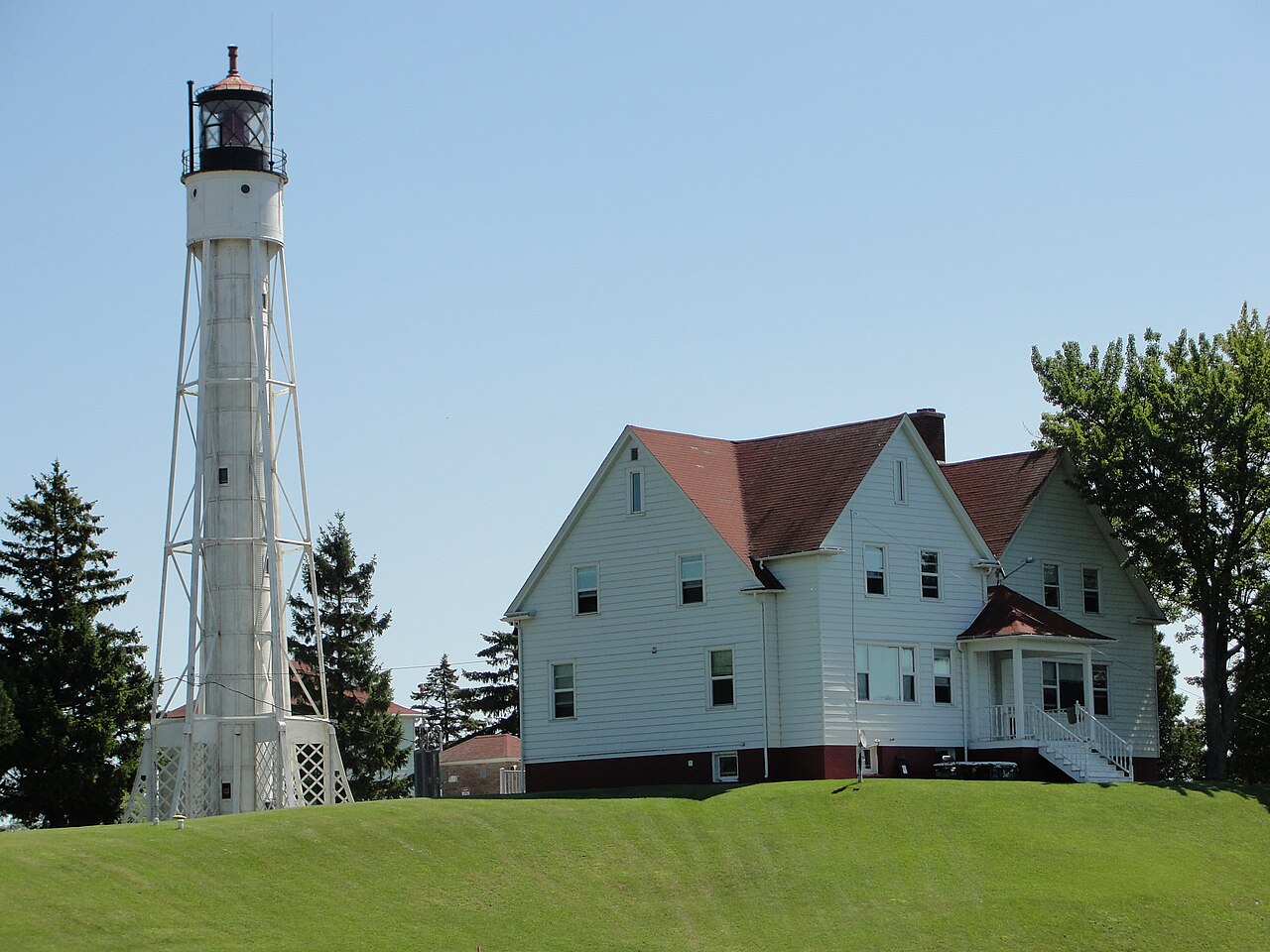 A tall white steel lighthouse tower beside a white house with a red roof