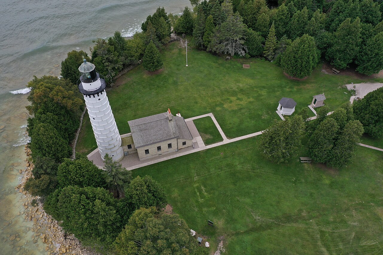 Aerial view of a white lighthouse and keeper's house on a wooded point beside the lake