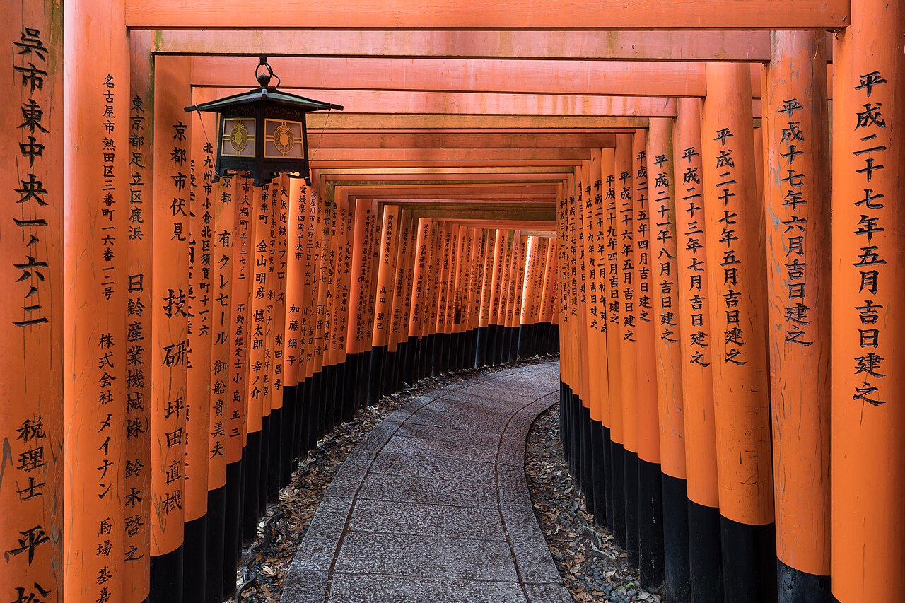 A path through a tunnel of bright orange gates with a hanging lantern