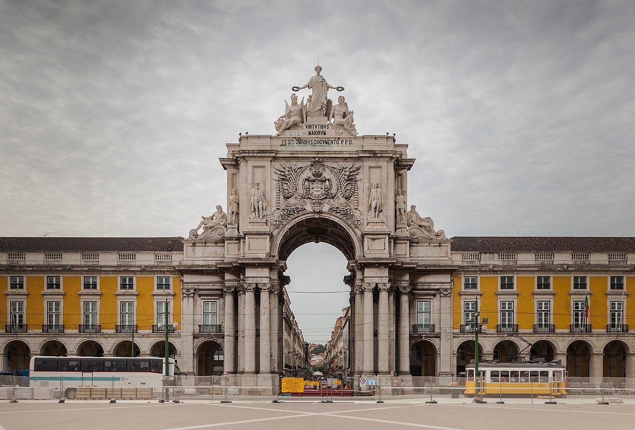 A grand stone triumphal arch at the end of a yellow-arcaded square