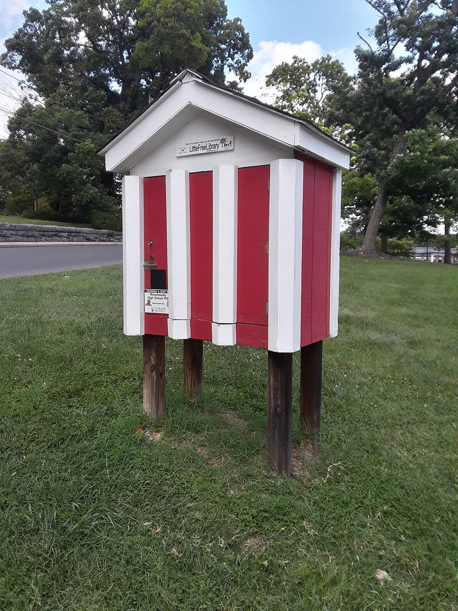 A red and white striped Little Free Library box on wooden posts on a lawn