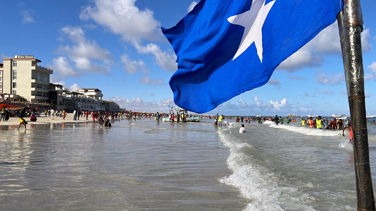 Crowds of people in the surf at Lido Beach in Mogadishu, with a Somali flag in the foreground