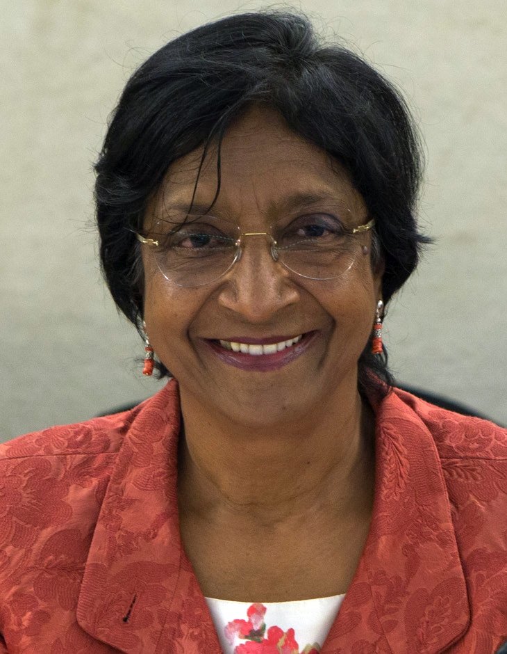 Navi Pillay, smiling, with short dark hair and glasses, wearing a red jacket