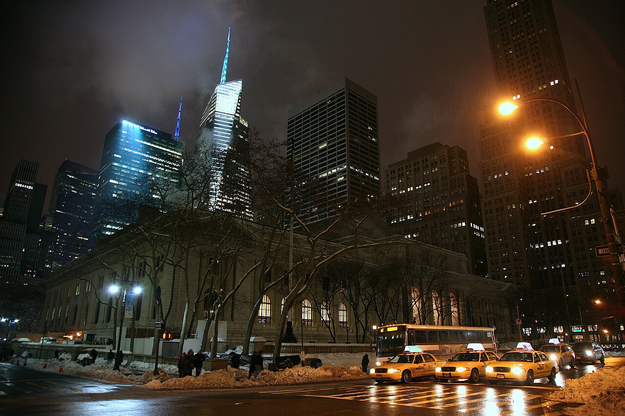 The New York Public Library's marble building lit at night, with yellow taxis on Fifth Avenue