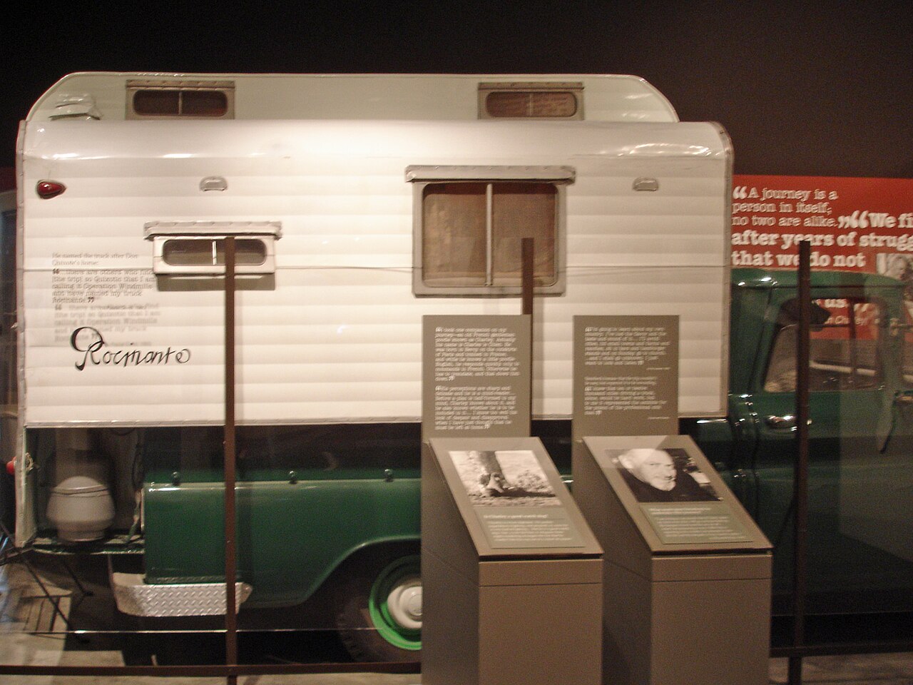 A green pickup truck with a white camper shell, the name Rocinante painted on its side, in a museum display