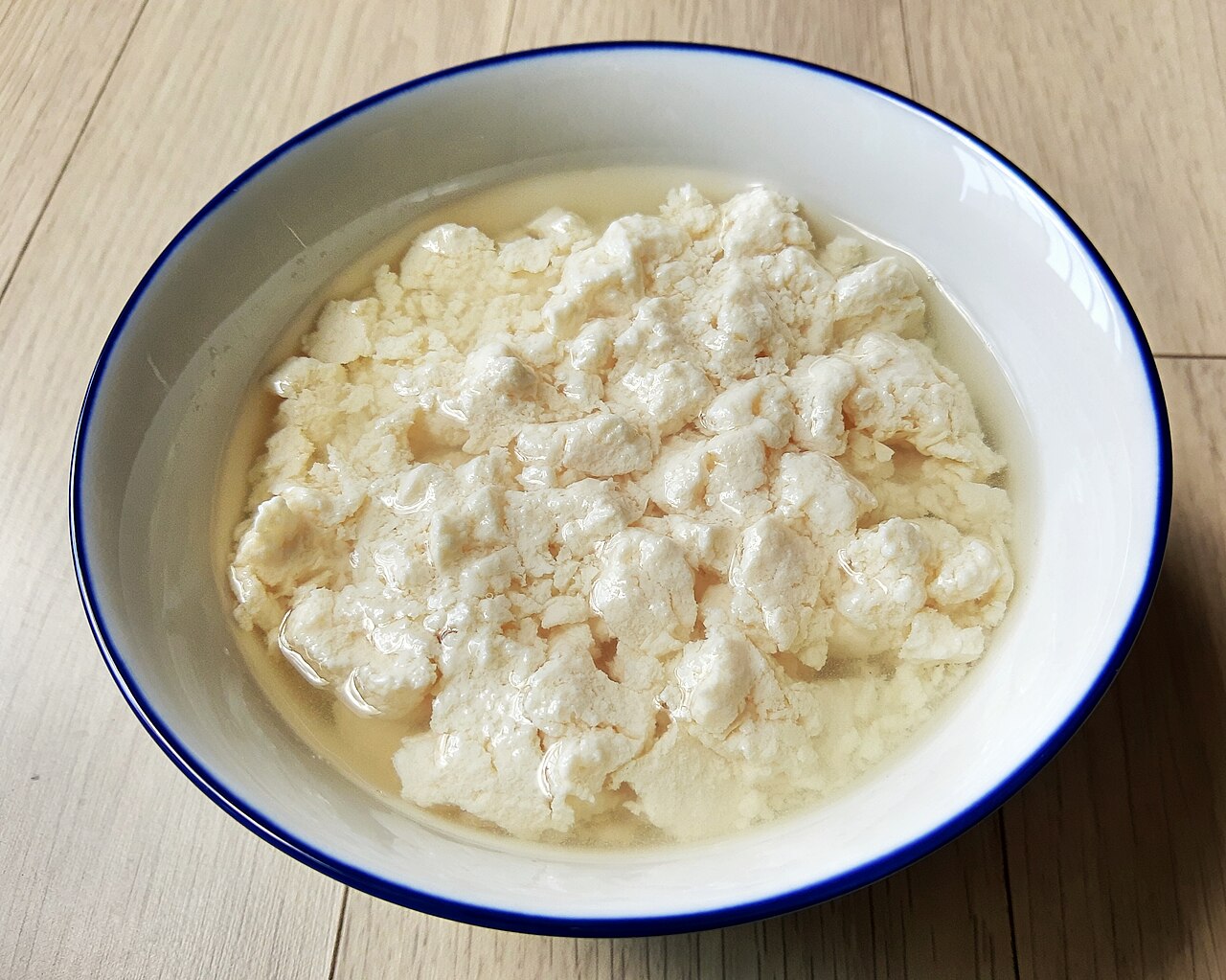A white bowl of fresh, soft, unpressed tofu curds in their liquid