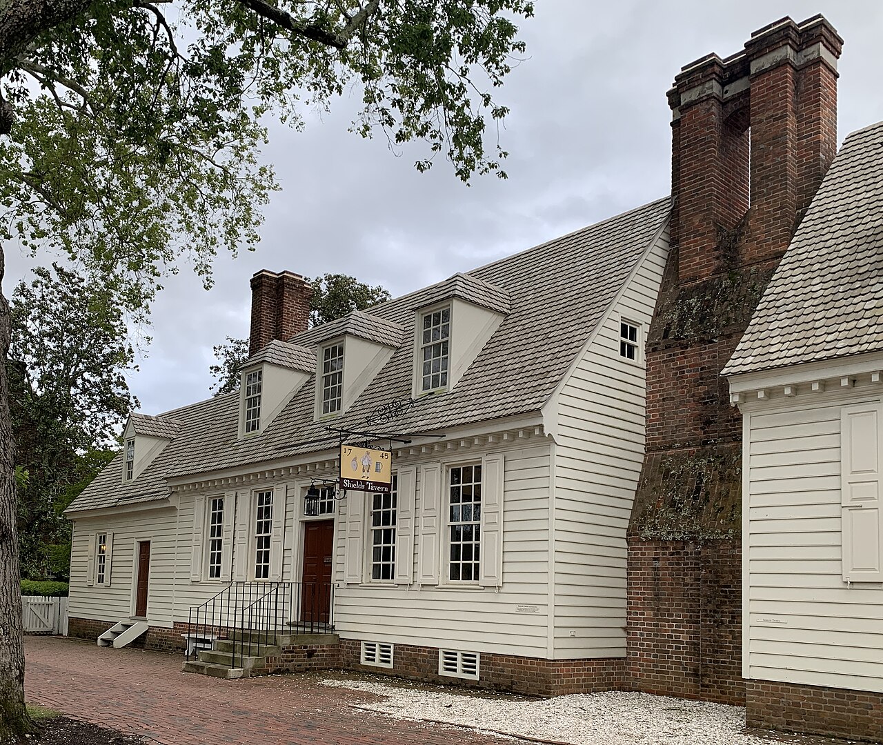 A white wooden colonial house with a tall brick chimney on a tree-lined street