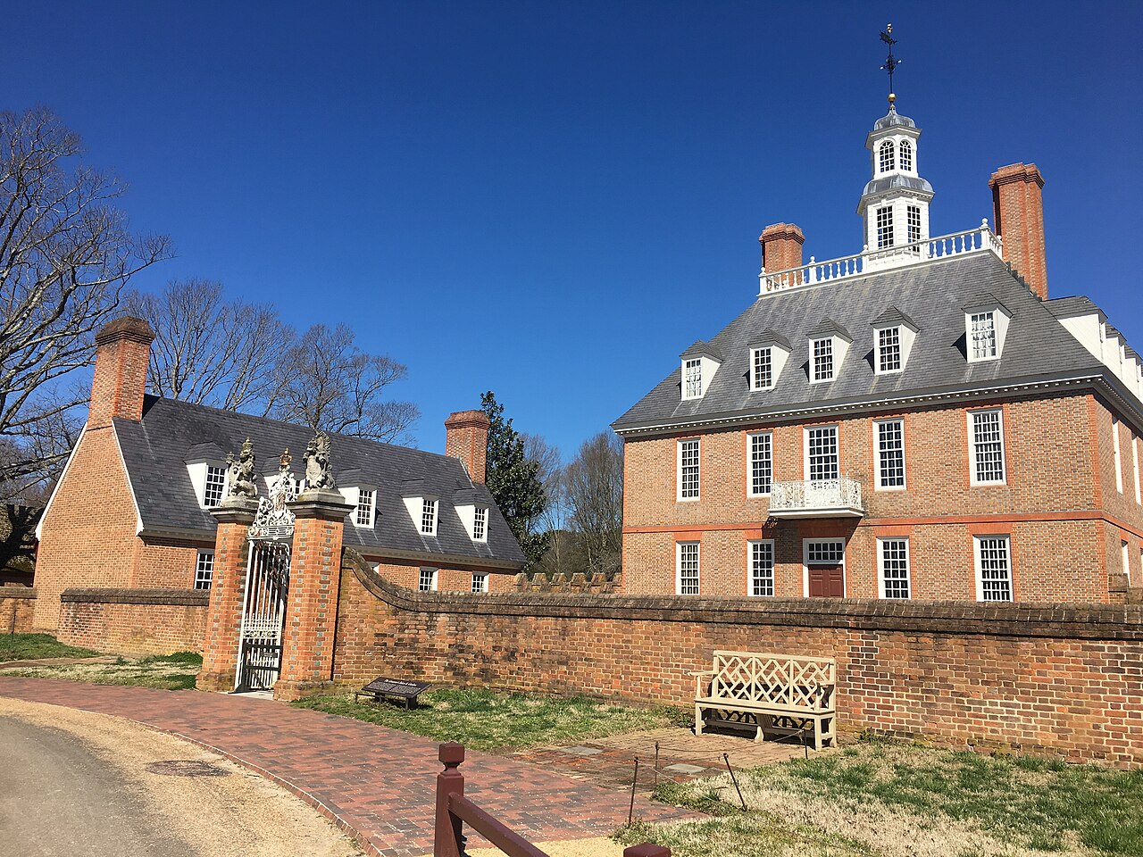 A red-brick mansion with a white cupola behind a brick wall and gate