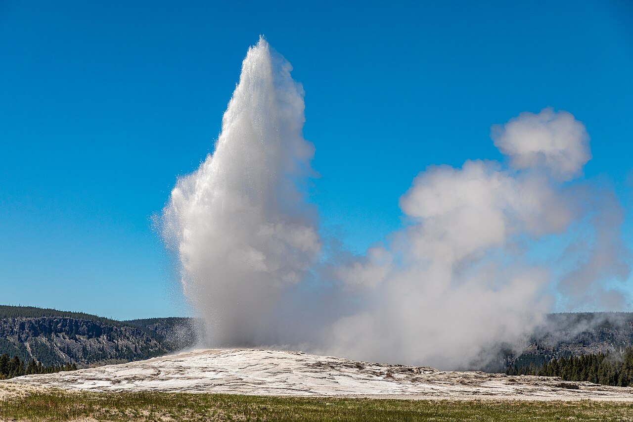 Old Faithful geyser erupting in a tall white column of steam under a blue sky