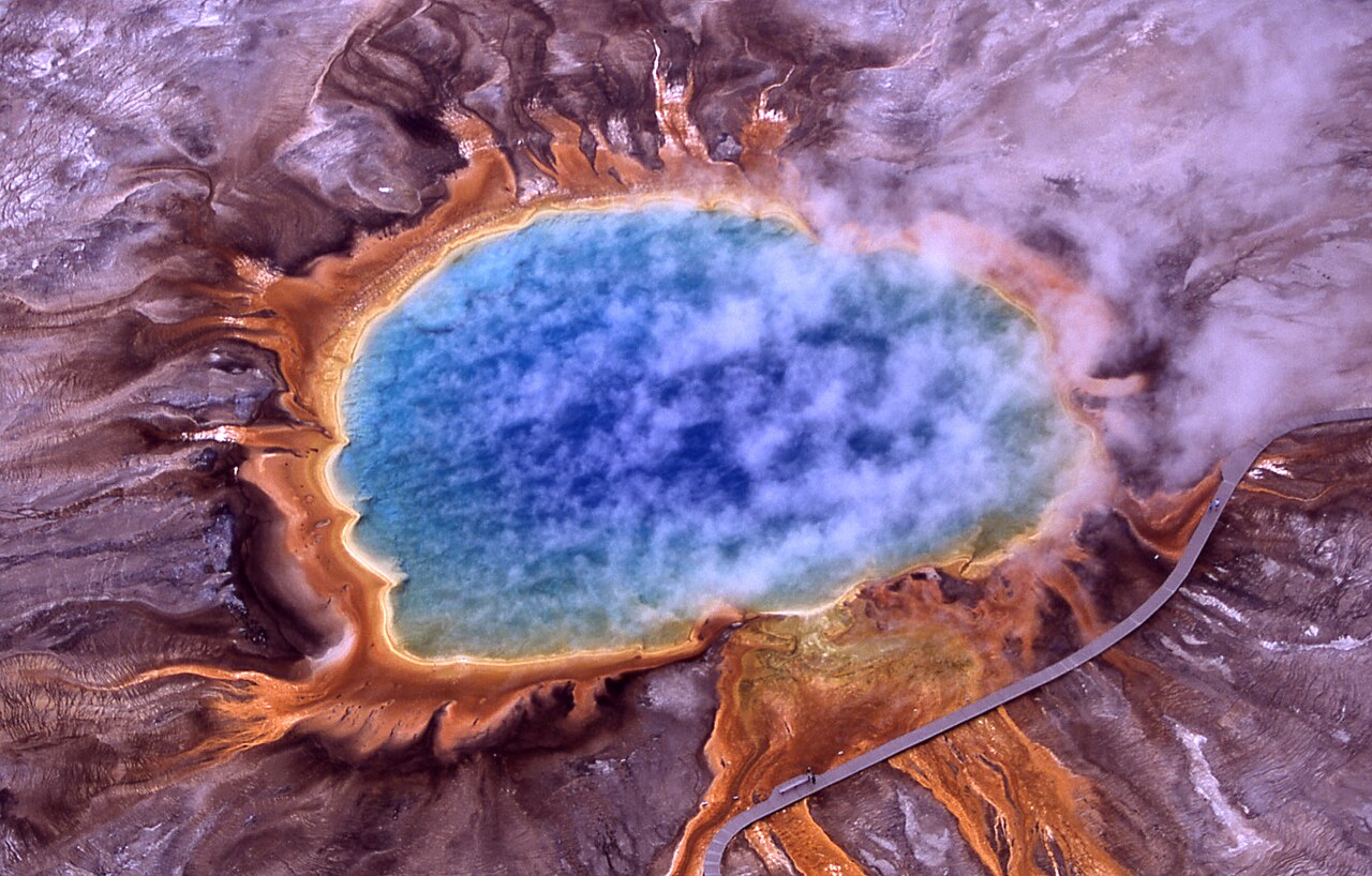 Aerial view of a huge hot spring, deep blue in the center with orange and yellow rings
