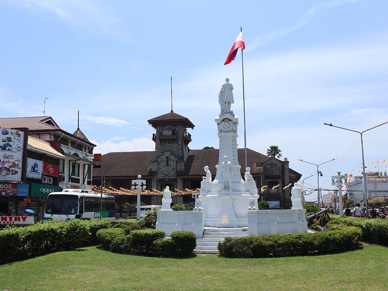 A white monument in a landscaped park in front of a historic city hall with a clock tower